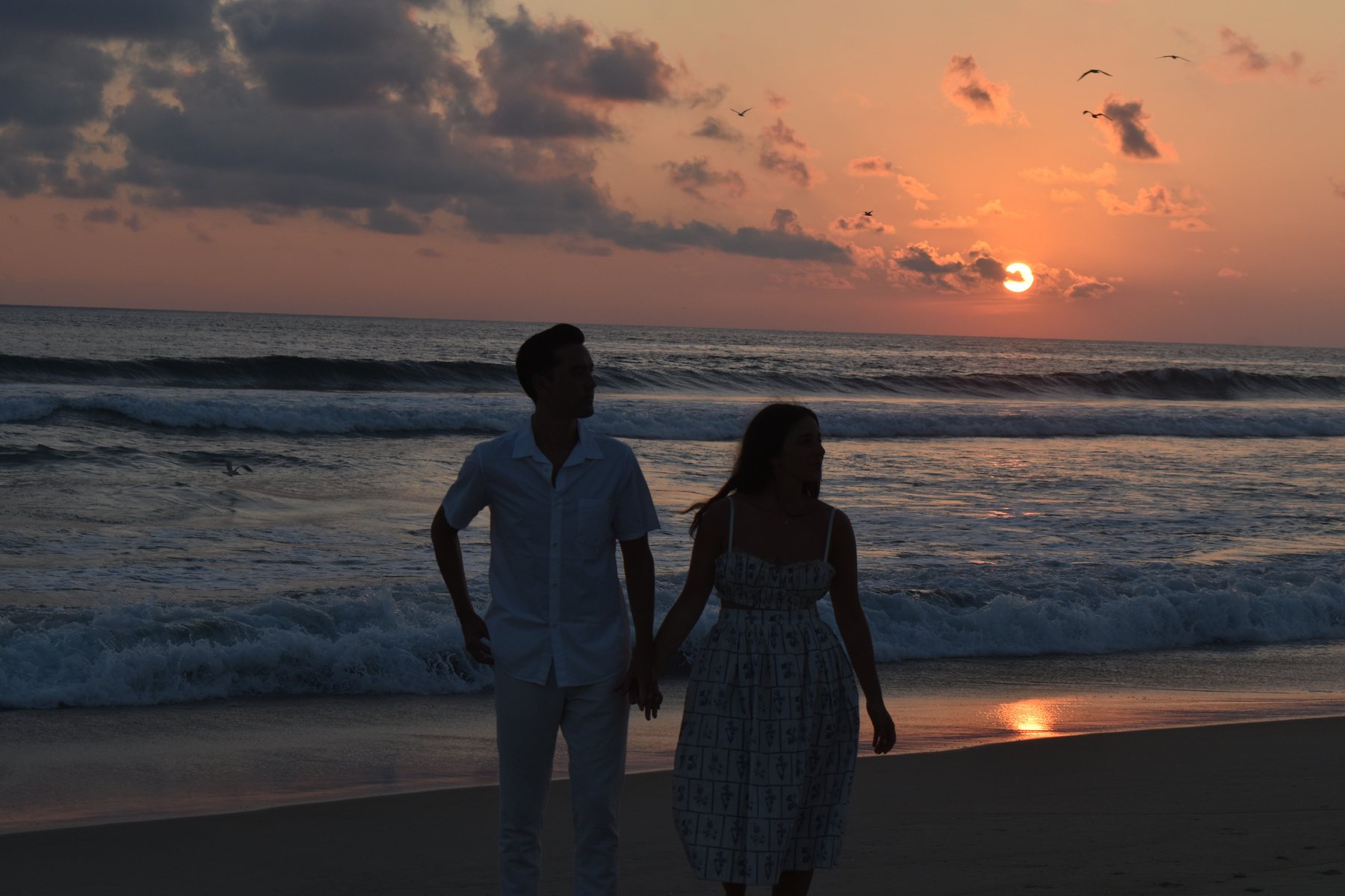 A couple walking the beach at sunset.